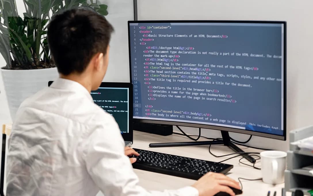 A developer at a desk writing server-side code across two monitors