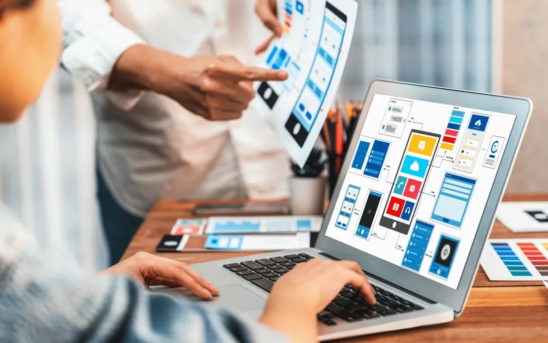 A team pointing at printed interface wireframes beside a laptop showing an app layout