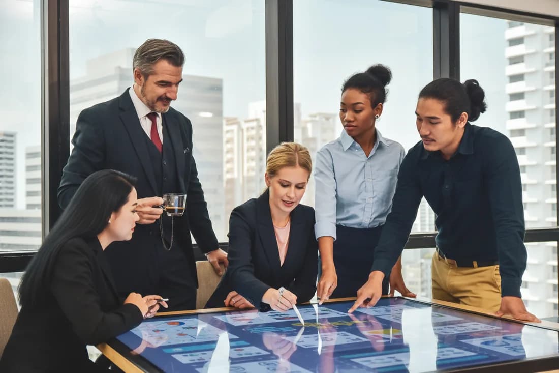 Five colleagues talking around a table in a city-view meeting room