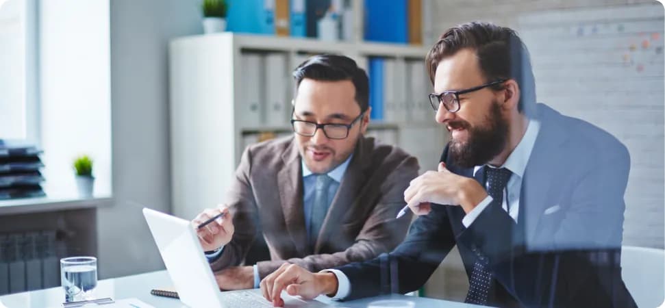 Two colleagues in suits discussing work at a laptop