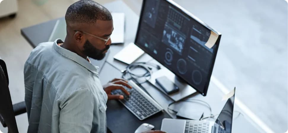 A developer working across two monitors showing dashboards