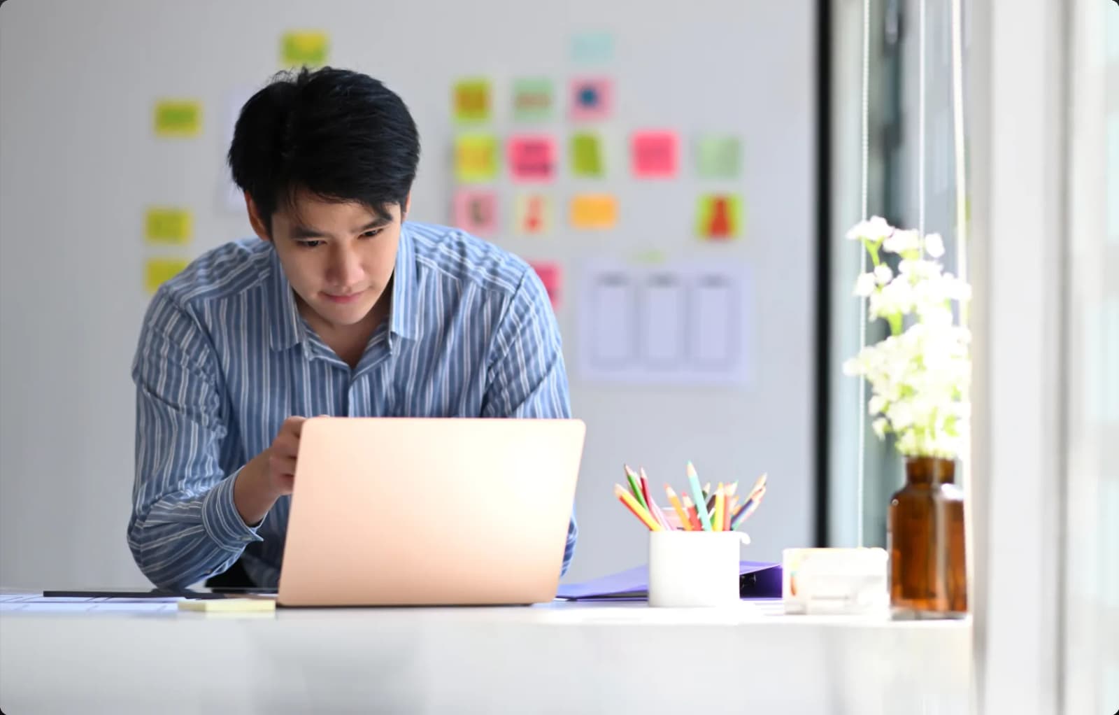 A developer working on a laptop at a desk in front of a wall of sticky notes